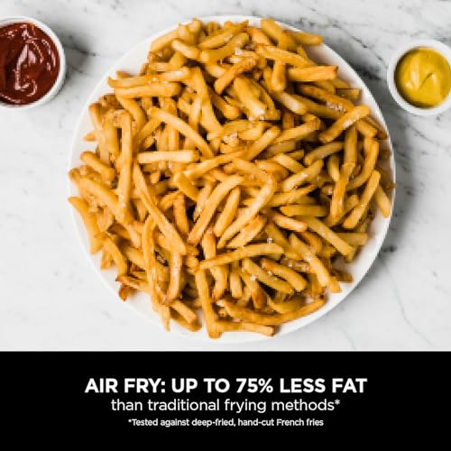 Air-fried French fries on a white plate with ketchup and mustard on a marble surface.
